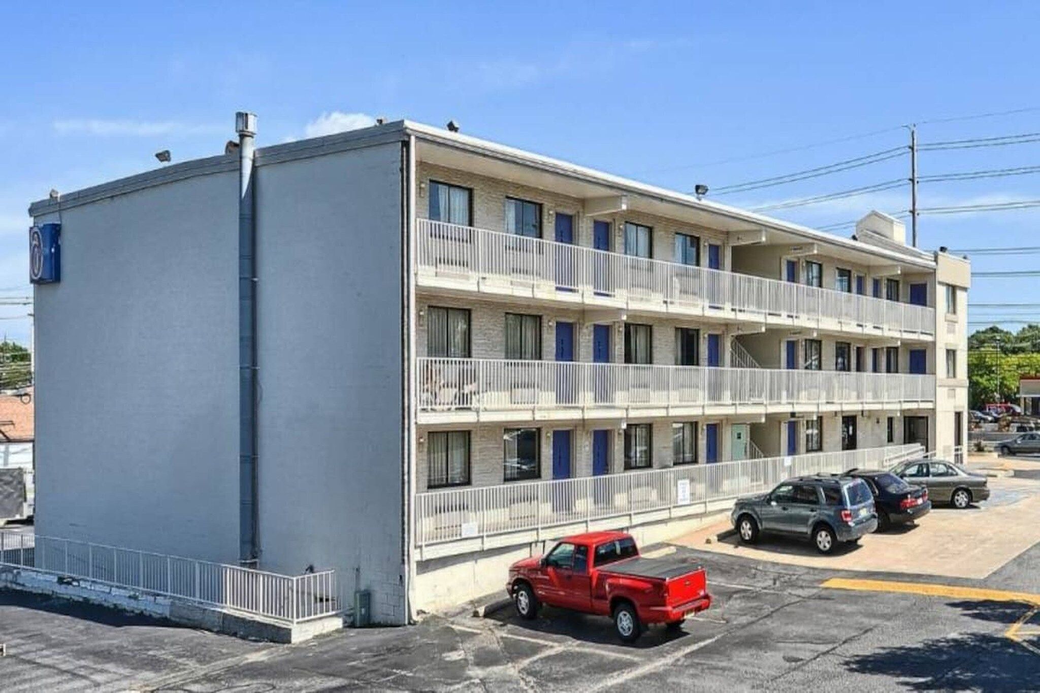 Een motel met meerdere verdiepingen, balkons en een parkeerplaats met verschillende auto's.