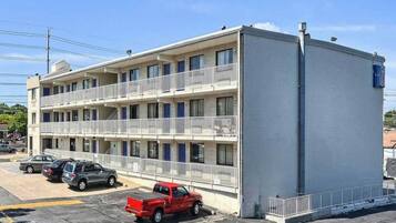 A multi-story motel with balconies, a parking lot, and a clear sky.