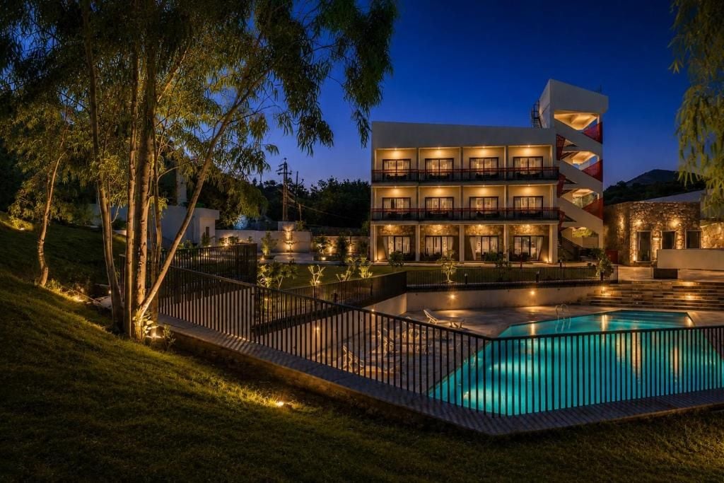 Un hotel de varios pisos con piscina, rodeado por una cerca y árboles.