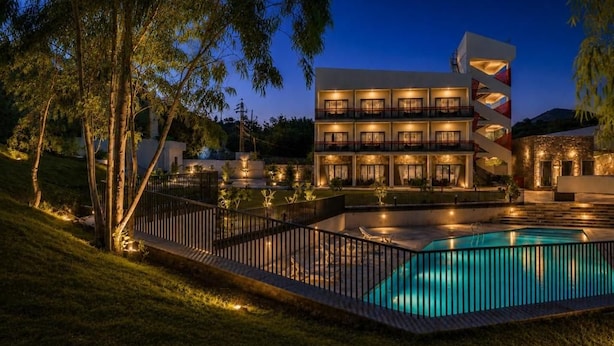 A multi-story hotel with a swimming pool, surrounded by a fence and trees. - Ullasa by Aranyam  Luxury Resort Udaipur (udiapur)