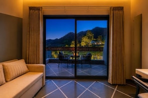 Una habitación con sofá, una mesa y un balcón con vistas a un paisaje montañoso.