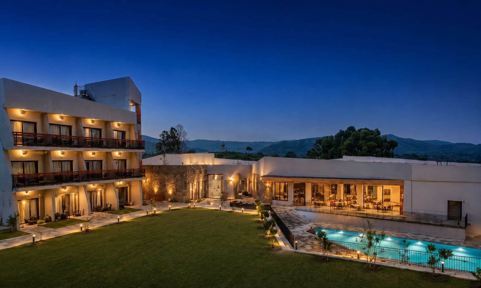 A modern hotel with multiple balconies, a swimming pool, and a well-maintained lawn.