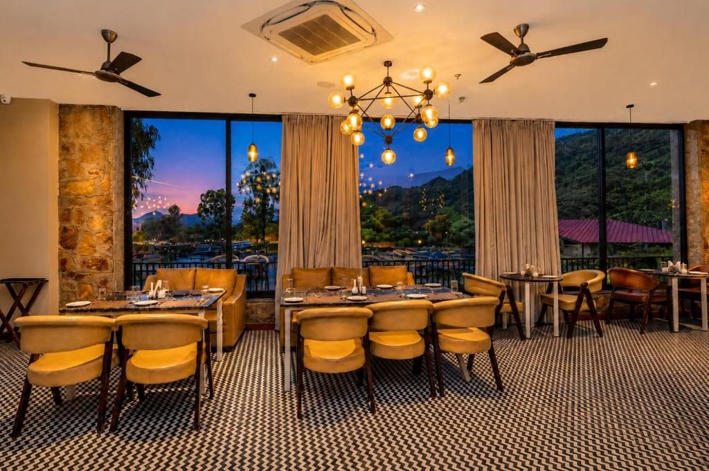 Un comedor con mesas y sillas, una araña y ventanas amplias con cortinas.