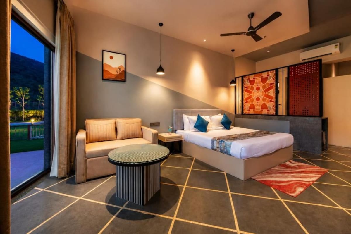 Habitación de hotel moderna con cama, sofá, una mesa redonda de centro y vistas al exterior.