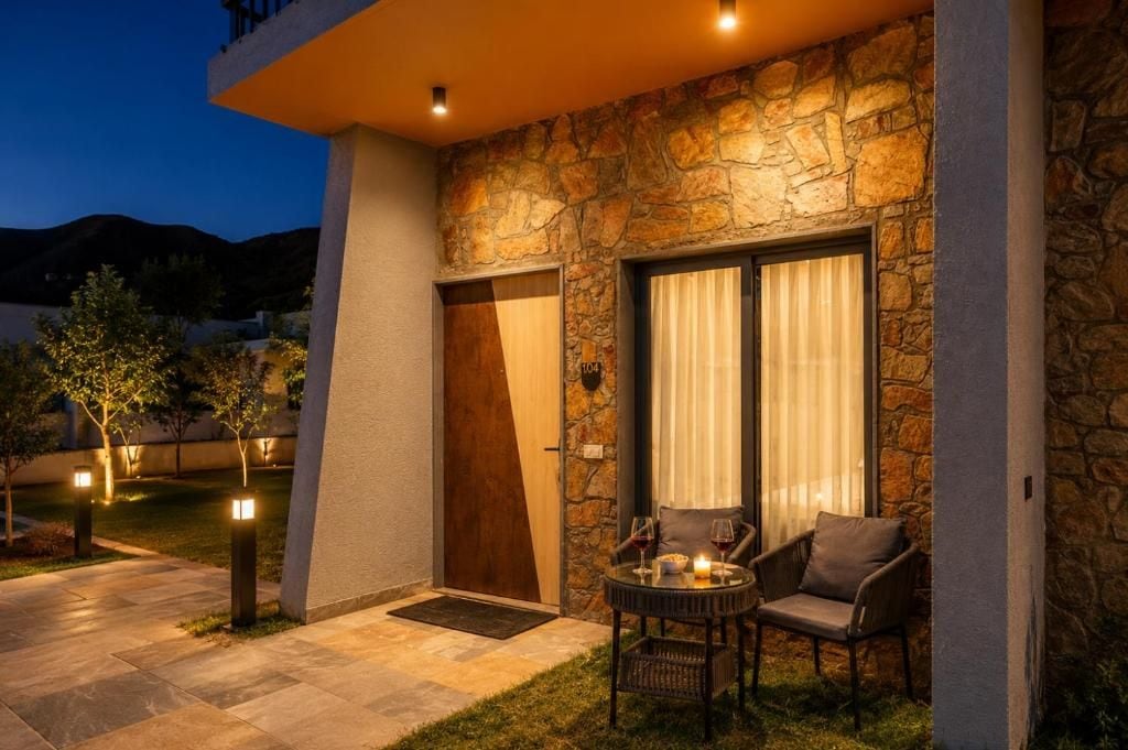 A stone exterior with a door and window, outdoor seating with chairs and a table, and a small garden area.