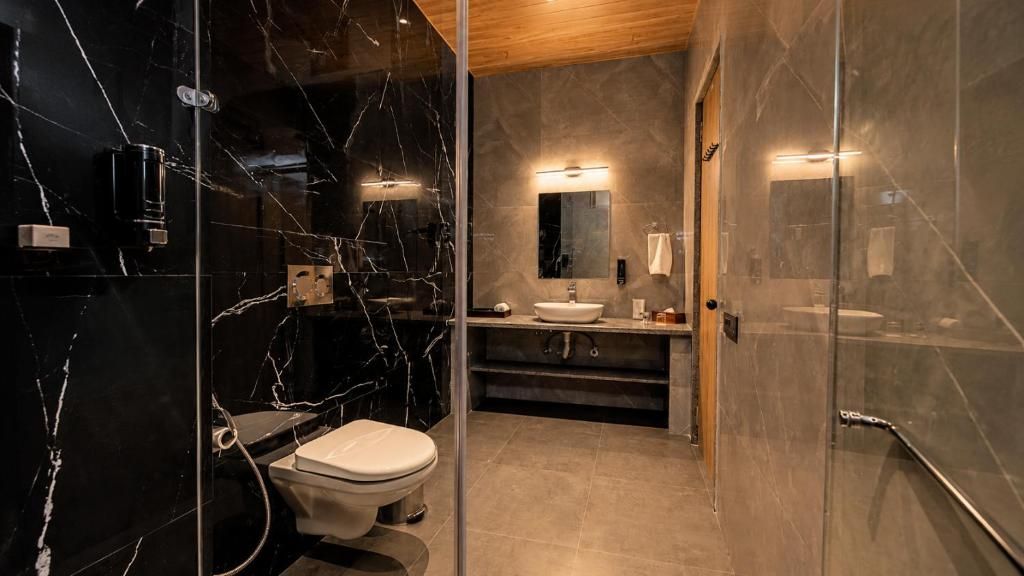 A modern bathroom with a glass shower enclosure, a marble-tiled wall, a wooden ceiling, and a white sink.