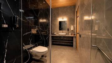 A modern bathroom with a glass shower enclosure, a marble-tiled wall, a wooden ceiling, and a white sink.