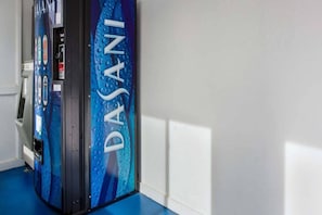 A vending machine with the brand 'DASANI' in a hallway with white walls and blue flooring.