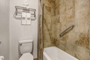 A bathroom with a toilet, a shower with a grab bar, and a towel rack with towels. - 2 Queen Beds | Smoking (Clovis NM)