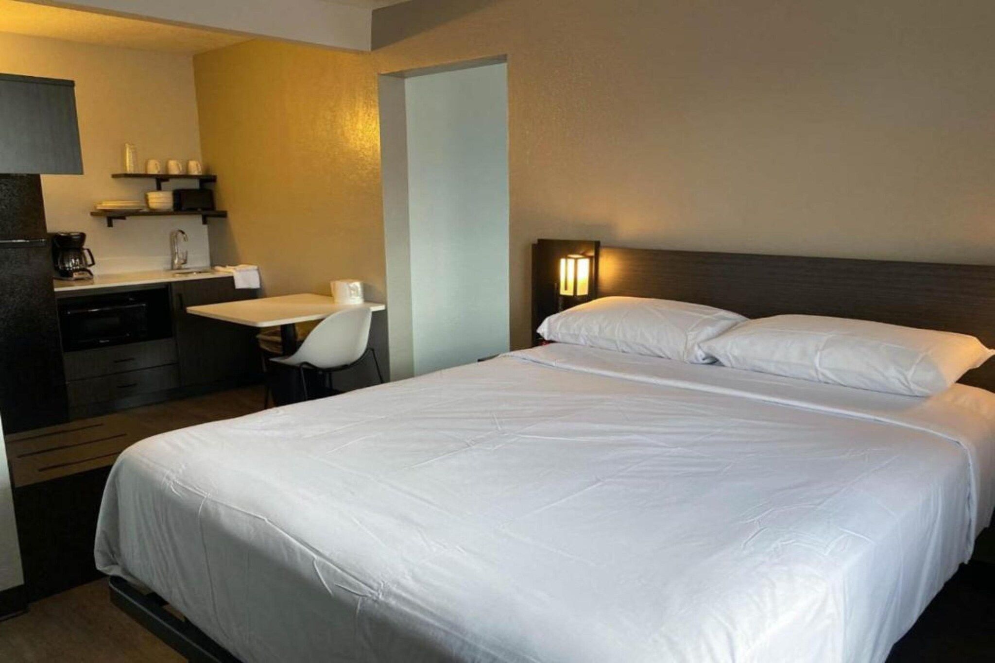 Een hotelkamer met een bed, een bureau, een stoel, een koffiezetapparaat en een nachtkastje.
