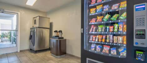 Máquina de vendas com lanches e um frigorífico numa divisão com pavimento em azulejos.
