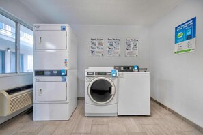 A laundry facility with stacked dryers, a front-loading washing machine, and instructional posters on the wall. - Sunny King Bed Suite|Pool|Free Wifi (Albuquerque NM)