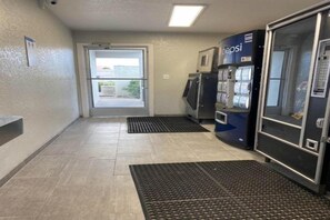 A hallway with a door leading outside, vending machines, and a doormat. - Spacious King Bed|Pool|Free Parking (Albuquerque NM)