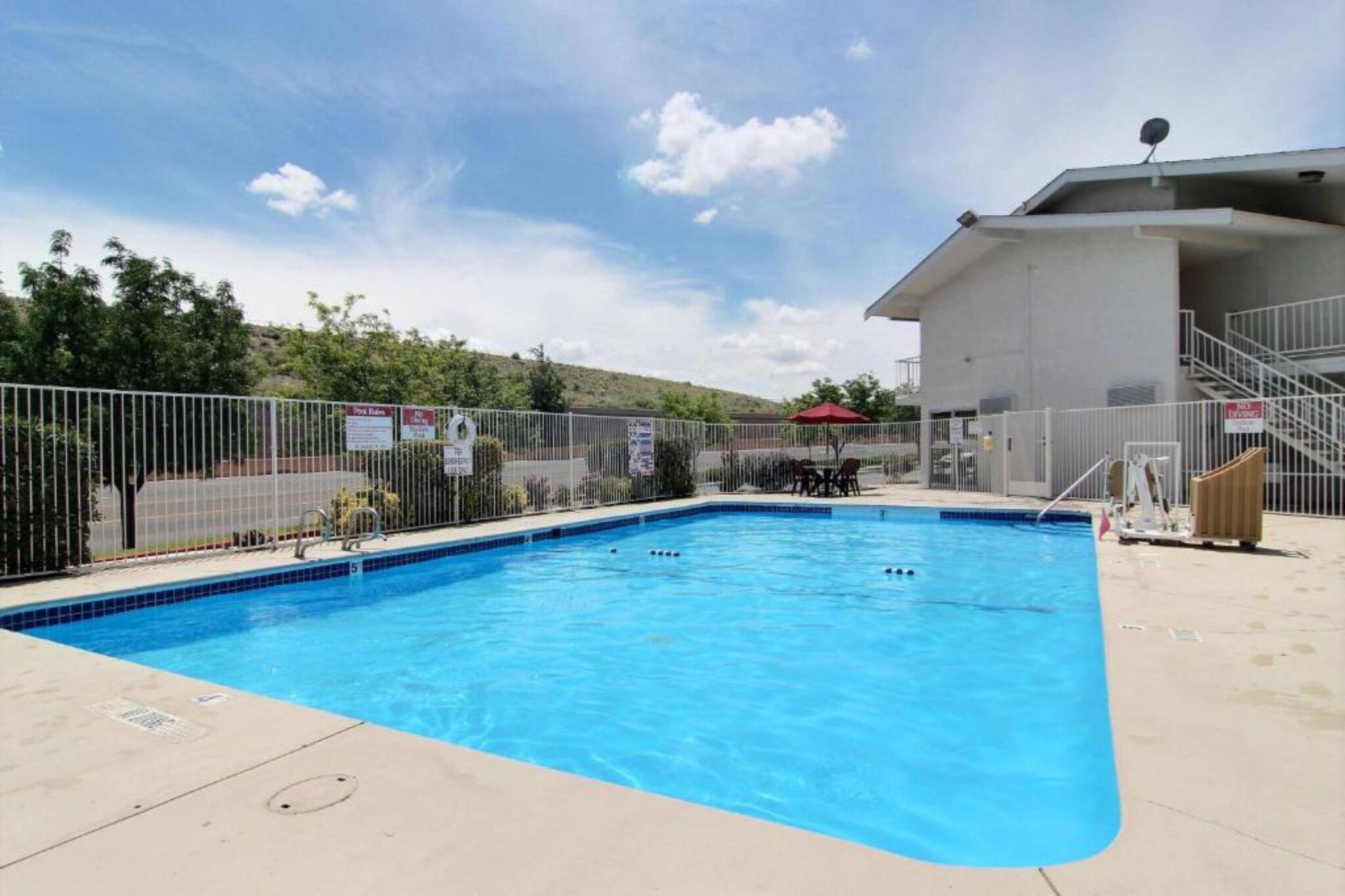 Une piscine entourée d’une clôture, un espace de repos couvert et un bâtiment équipé d’une antenne parabolique.