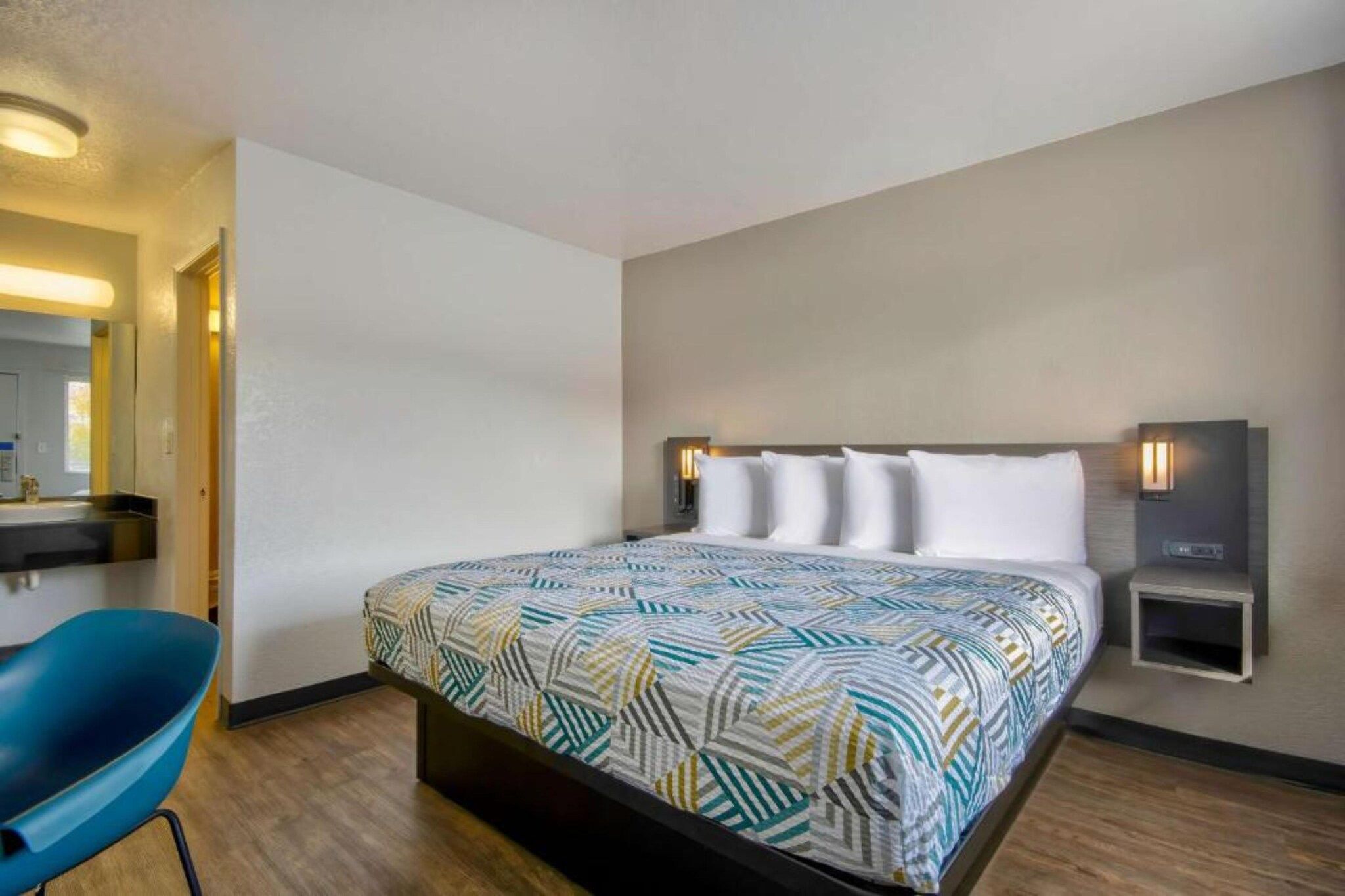 Une chambre d’hôtel avec un lit, une chaise, une table de chevet et une lampe fixée au mur.