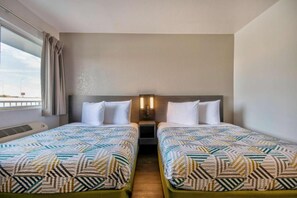 Ein Hotelzimmer mit zwei Betten, einem Fenster mit Vorhängen, einem Wandheizkörper und einem Nachttisch mit einer Lampe.