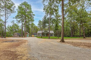 A residential property with a gravel driveway leading to a house surrounded by tall trees. - Wooded Piney Woods Tiny Home w/ King Loft & Deck (Willis)