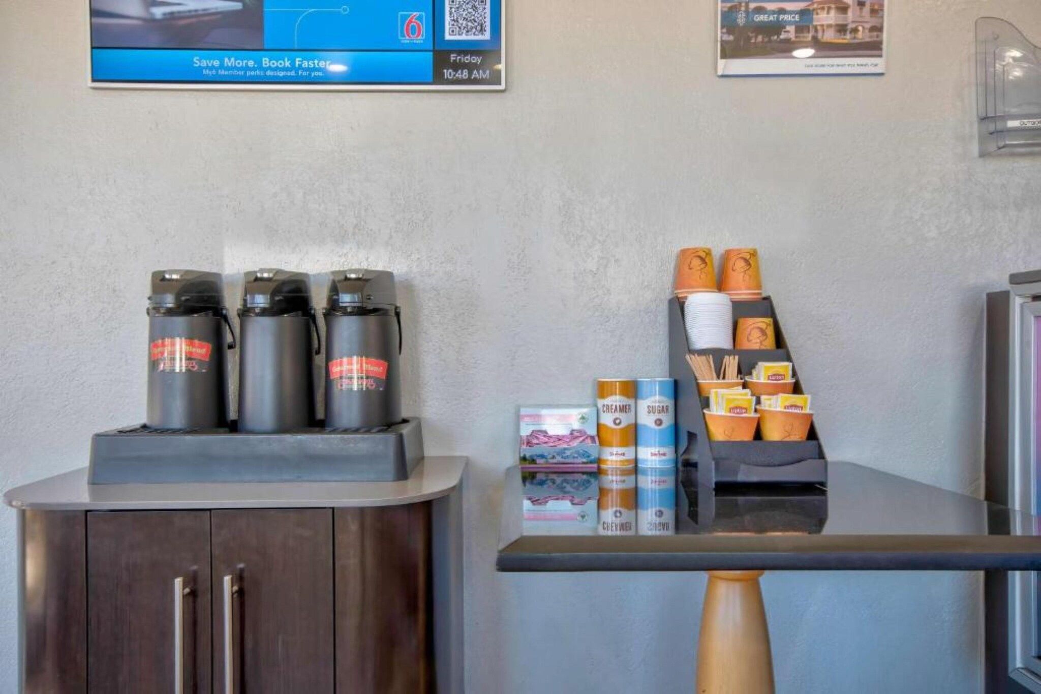 Una estación de café con mostrador, un armario con cafetera y una exhibición de tazas y recipientes para café.