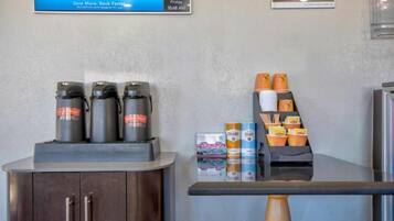 Una estación de café con mostrador, un armario con cafetera y una exhibición de tazas y recipientes para café.