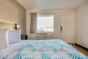 Ein Hotelzimmer mit Bett, einem Vorhangfenster, einer Tür und einer Wand-Klimaanlage.