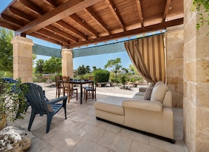 Une terrasse extérieure dotée d’une pergola en bois, de piliers en pierre, d’un canapé beige et d’une table à manger avec des chaises.