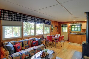 A cozy living room with a sofa, dining table, and chairs, wooden floors, and large windows with curtains. - Sibley Shores Waterfront Cabin w/ Dock & 28 Acres (Pequot Lakes)