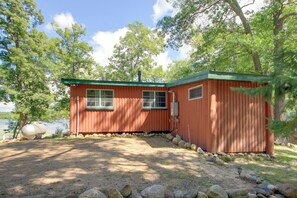 A small, single-story cabin with a green roof, situated by a body of water, surrounded by trees. - Sibley Shores Waterfront Cabin w/ Dock & 28 Acres (Pequot Lakes)