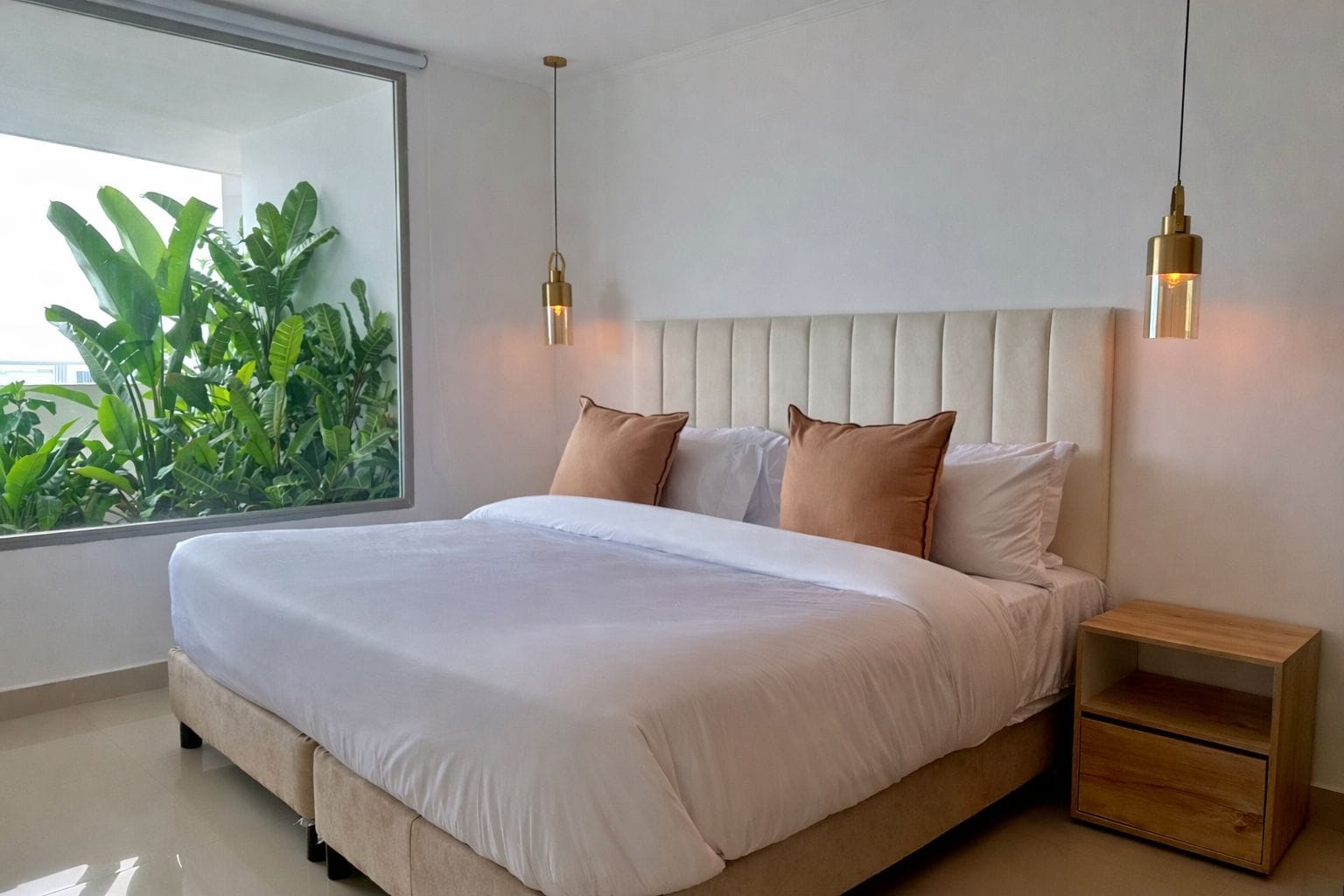 A modern bedroom with a large bed, two bedside tables, and a view of greenery outside.