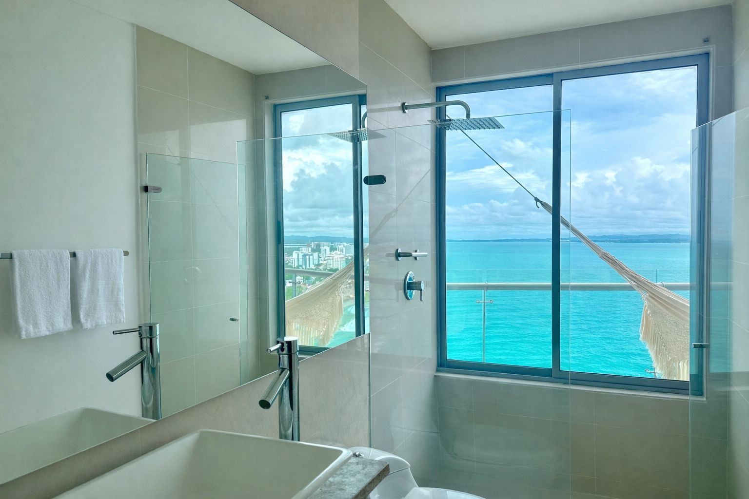 Un baño moderno con cabina de ducha de vidrio, un espejo grande y vistas al océano.