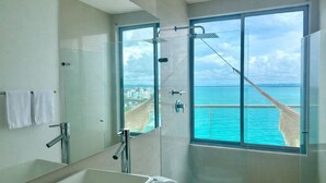 Uma casa de banho moderna com cabine de duche em vidro, um espelho grande e vista para o oceano.