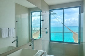 Un baño moderno con cabina de ducha de vidrio, un espejo grande y vistas al océano.