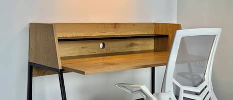 A wooden desk with a mesh chair, a drawer, and three pendant lights.