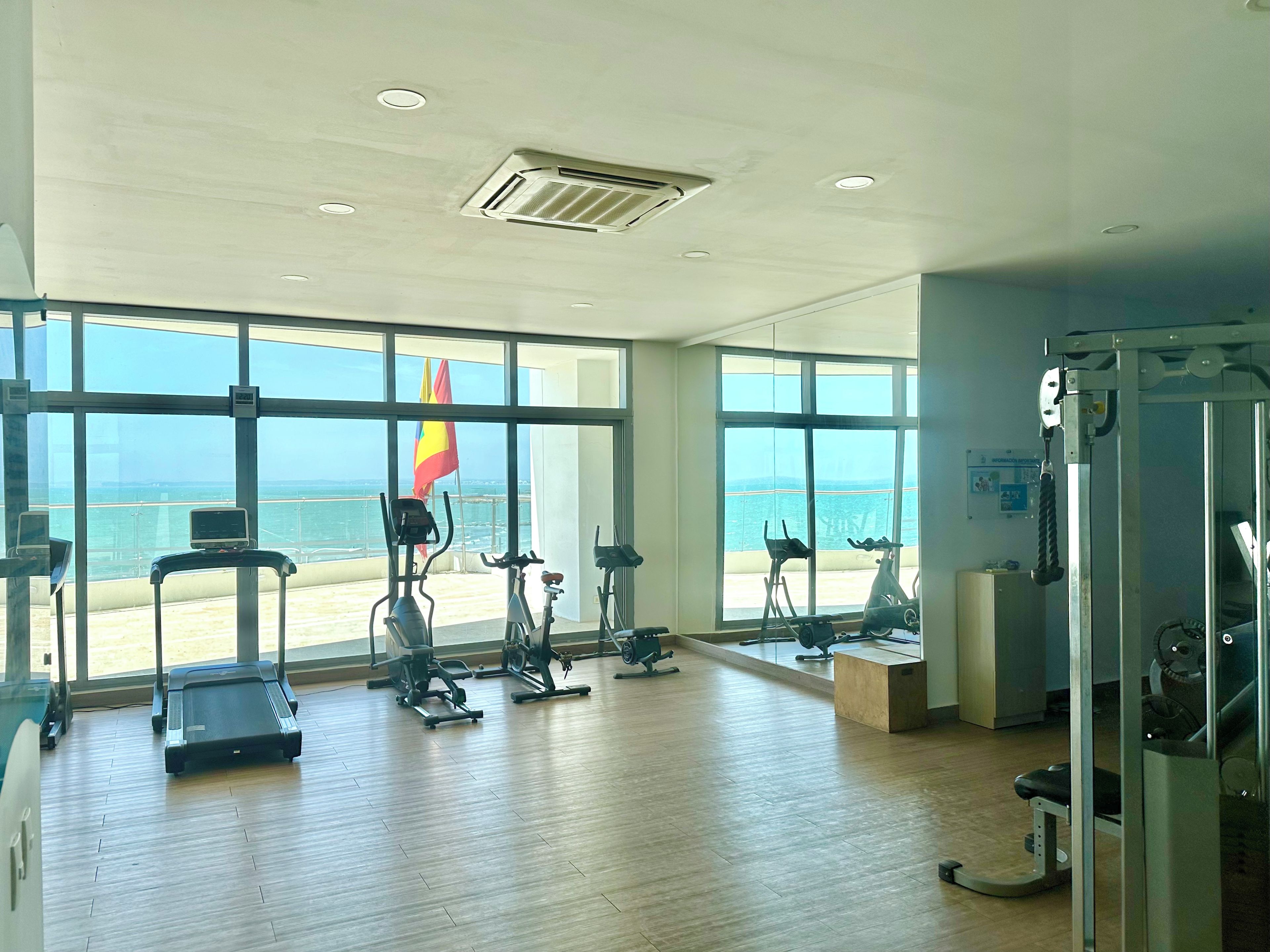 Une salle de sport spacieuse, dotée de grandes fenêtres, de divers appareils d’exercice et offrant une vue sur la mer.