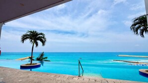 Vista da piscina com céu azul claro, praia de areia e palmeiras.
