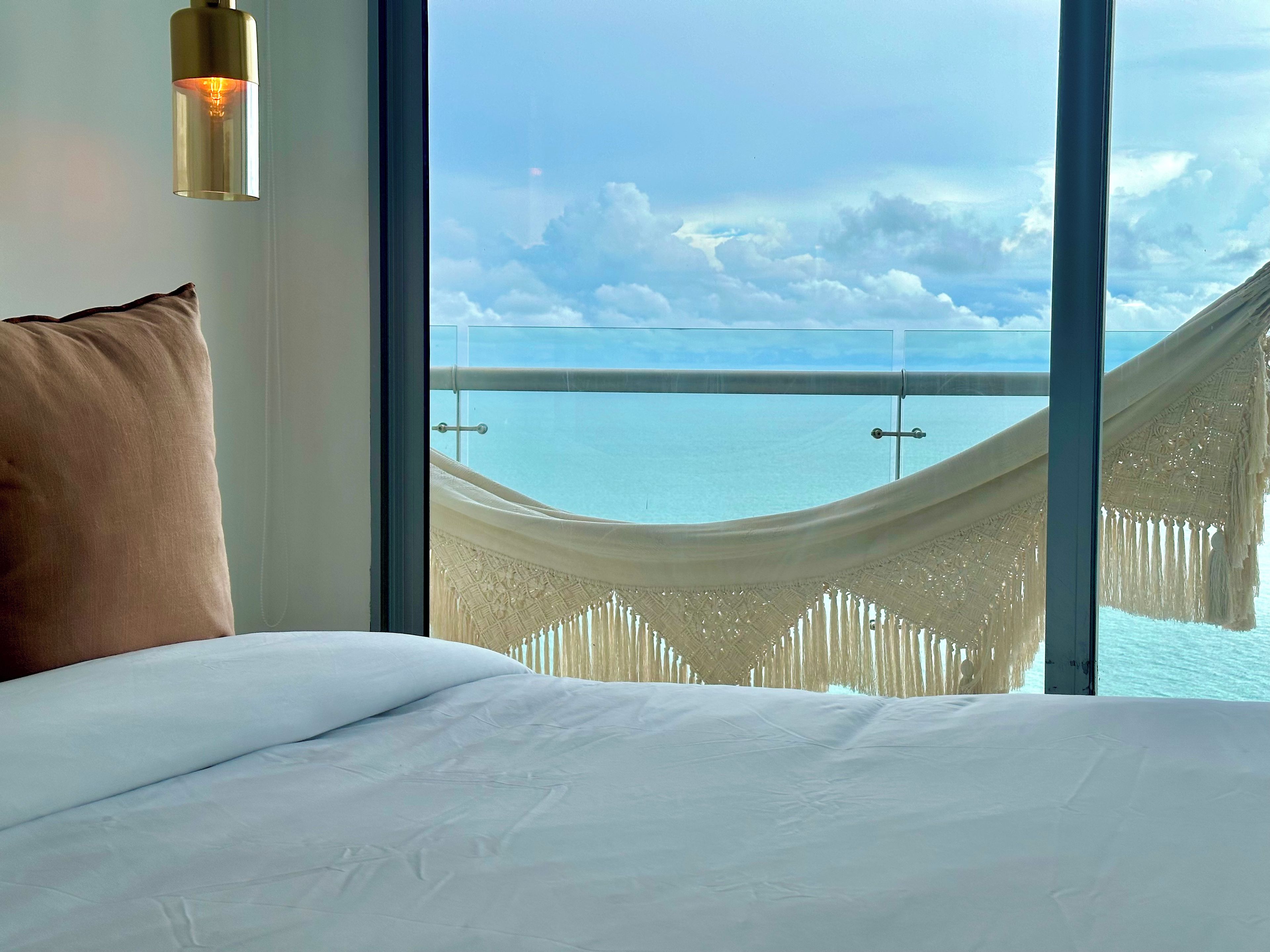 Ein Bett mit Blick auf das Meer durch ein Fenster, inklusive Hängematte.