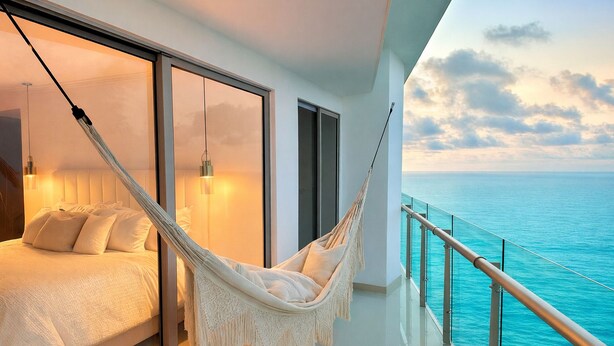 Uma varanda com vista para o oceano, uma rede e uma cama com almofadas.