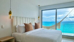 Quarto com cama grande, mesa de cabeceira, vista para o oceano pela janela e rede do lado de fora.
