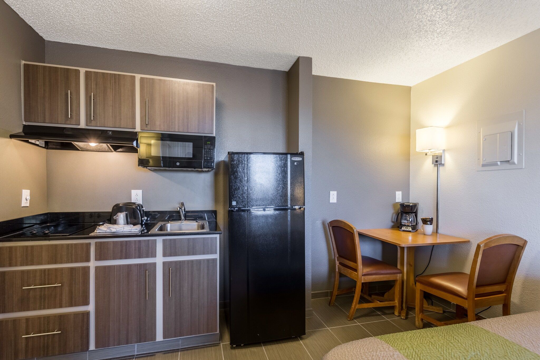 A compact kitchenette with a microwave, refrigerator, and stove. There is a small dining area with two chairs and a table.