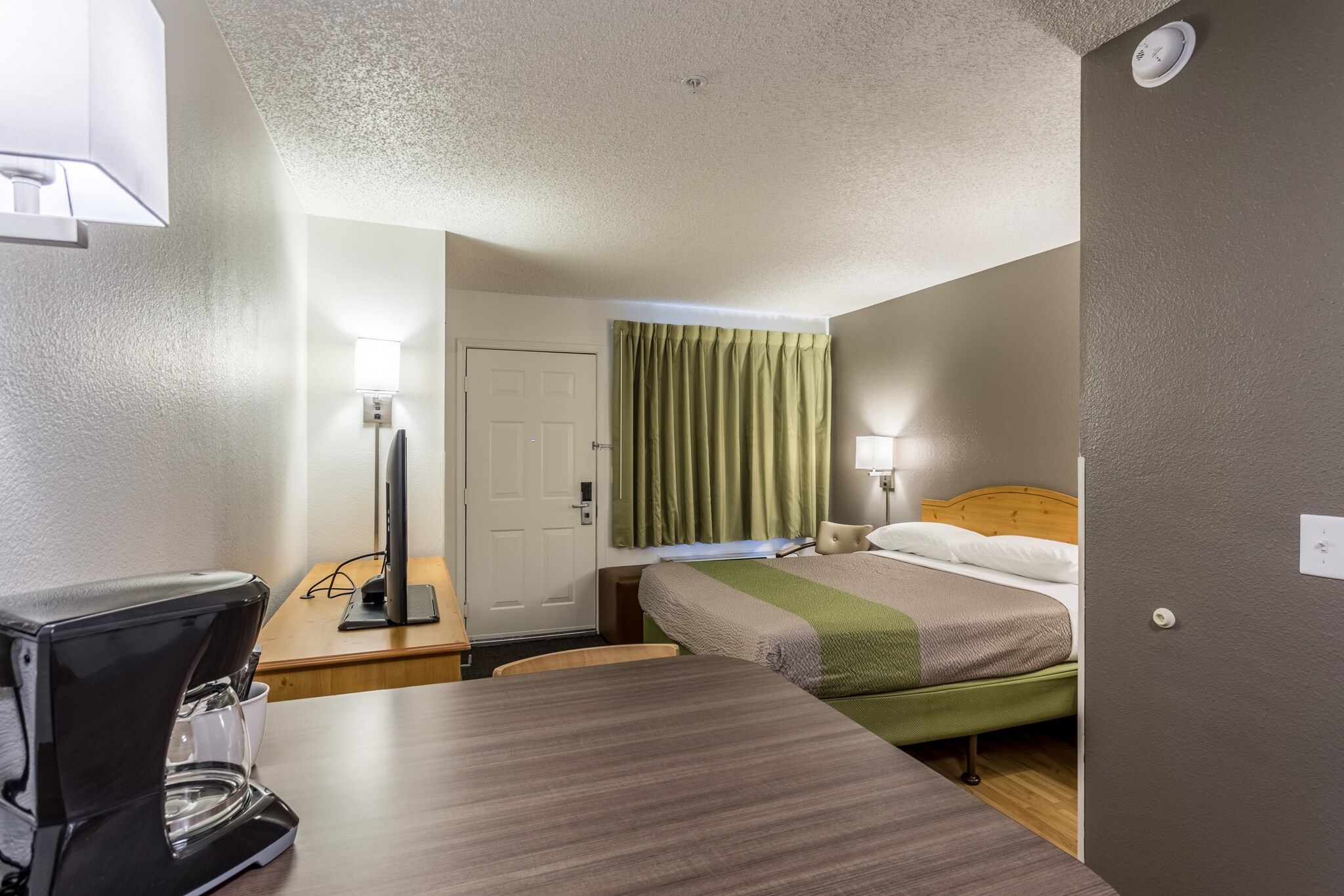 A hotel room with a bed, bedside table, lamp, and a coffee maker.