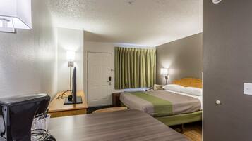 A hotel room with a bed, bedside table, lamp, and a coffee maker.