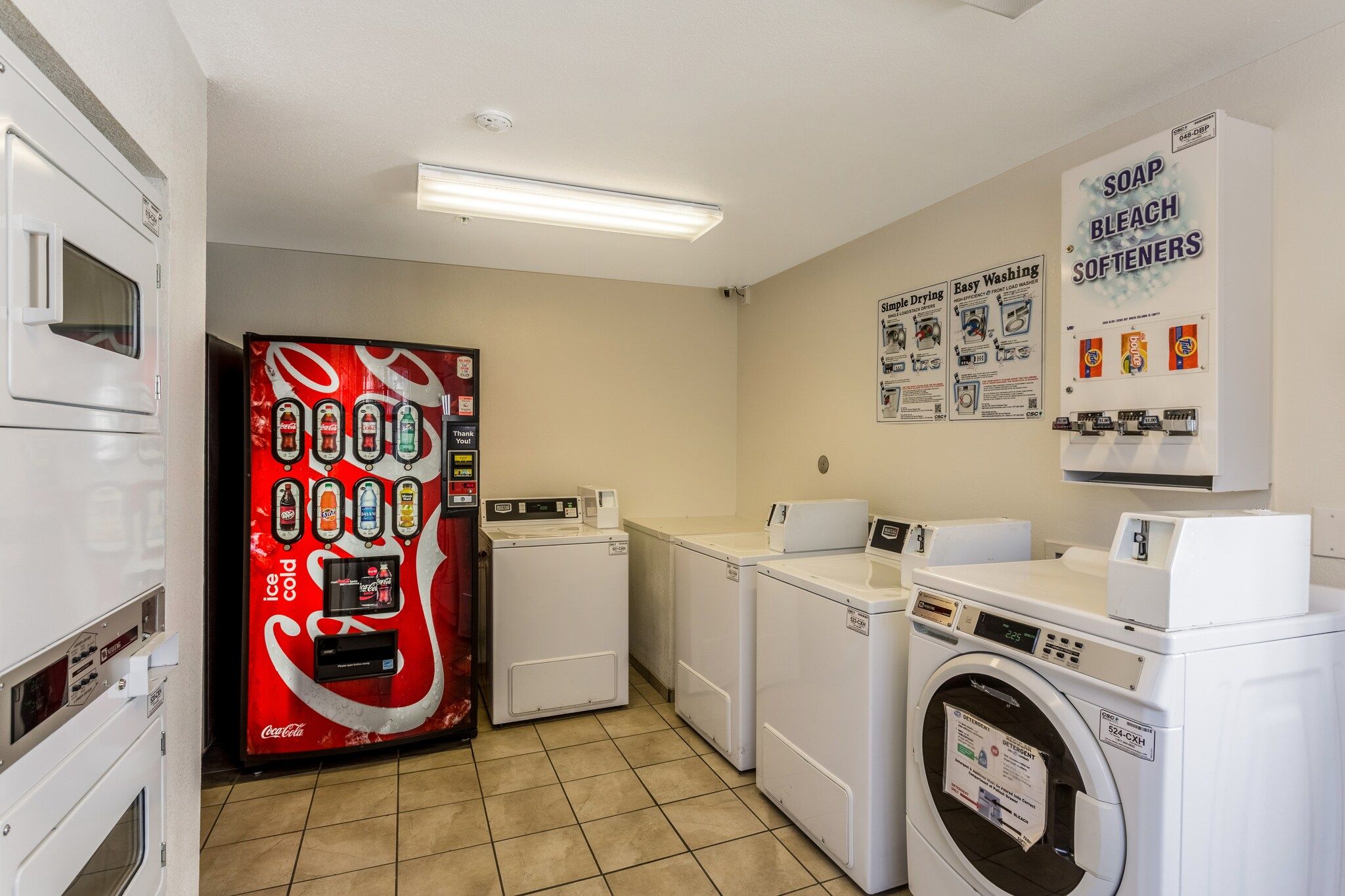 A laundry facility with a vending machine, dryers, washers, and detergent dispensers.