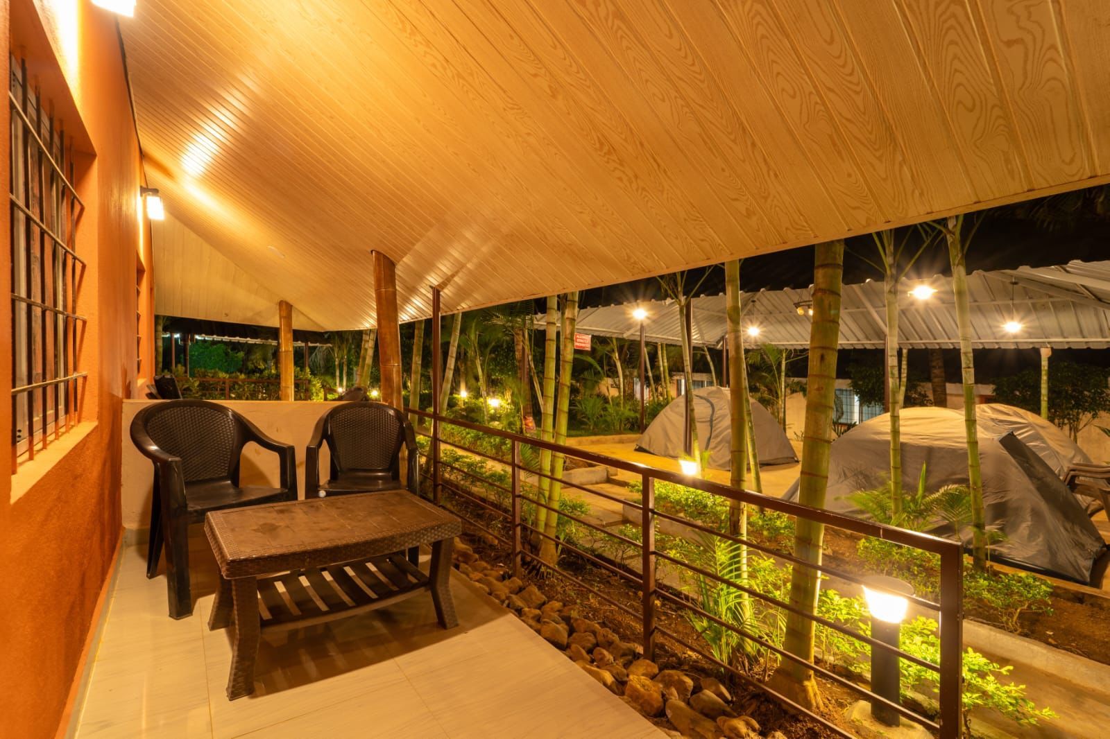 An outdoor covered area with seating, a railing, and a view of the surrounding garden at night.