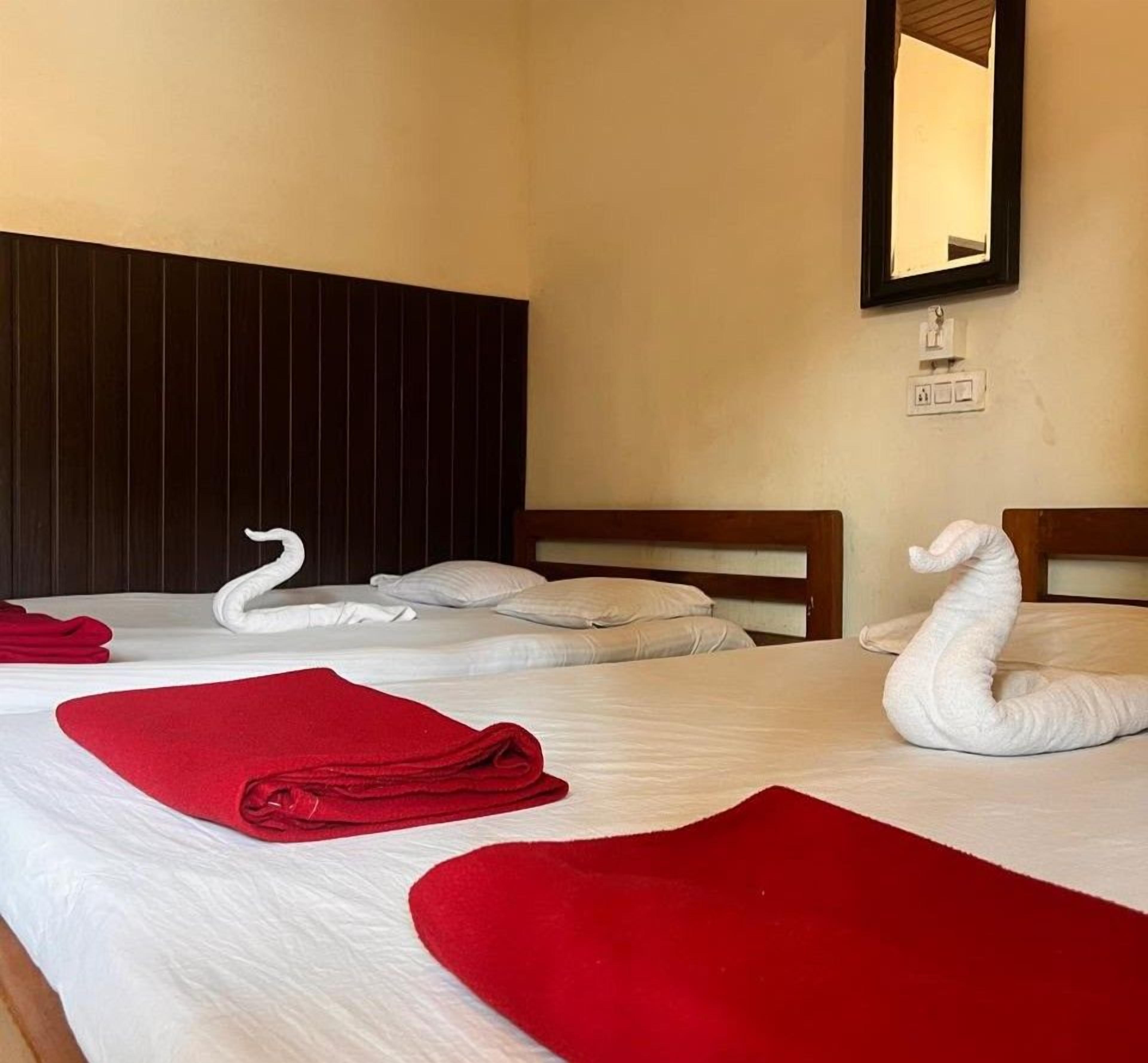 A hotel room with two beds, each with a white swan-shaped towel and a red towel.