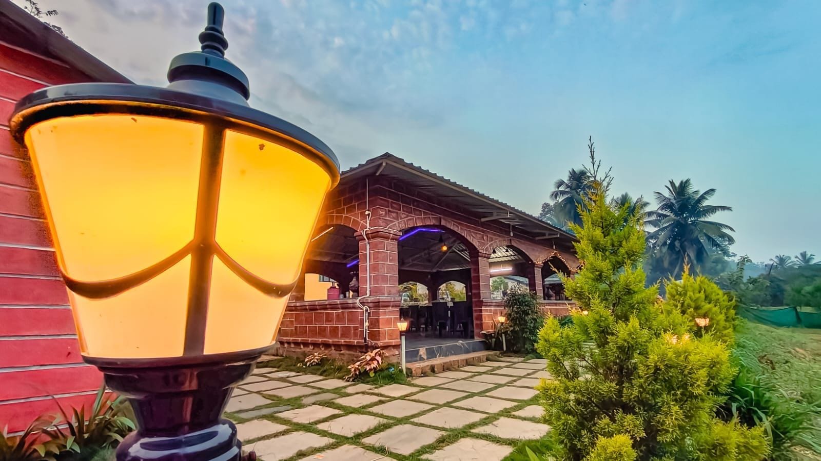 A building with a brick facade, a covered outdoor area with arches, and a large, illuminated street lamp.