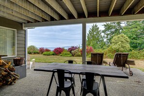 An outdoor patio with a table and chairs, a covered area with a view of the landscape, and a pile of firewood. - Puget Sound Views & Patio: Point No Point Apt (Hansville)