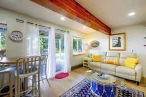 A room with a dining table, chairs, a sofa with yellow cushions, a drum, and a clock on the wall. - Puget Sound Views & Patio: Point No Point Apt (Hansville)