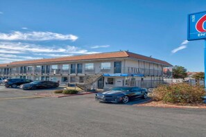 A motel with a two-story structure, a parking lot with several cars, and a clear blue sky. - 1 Full Bed | Non-smoking (Albuquerque)