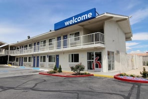 A hotel with a 'welcome' sign, a parking lot, and a building with multiple doors and windows. - 1 King Bed | Non-Smoking (Albuquerque)