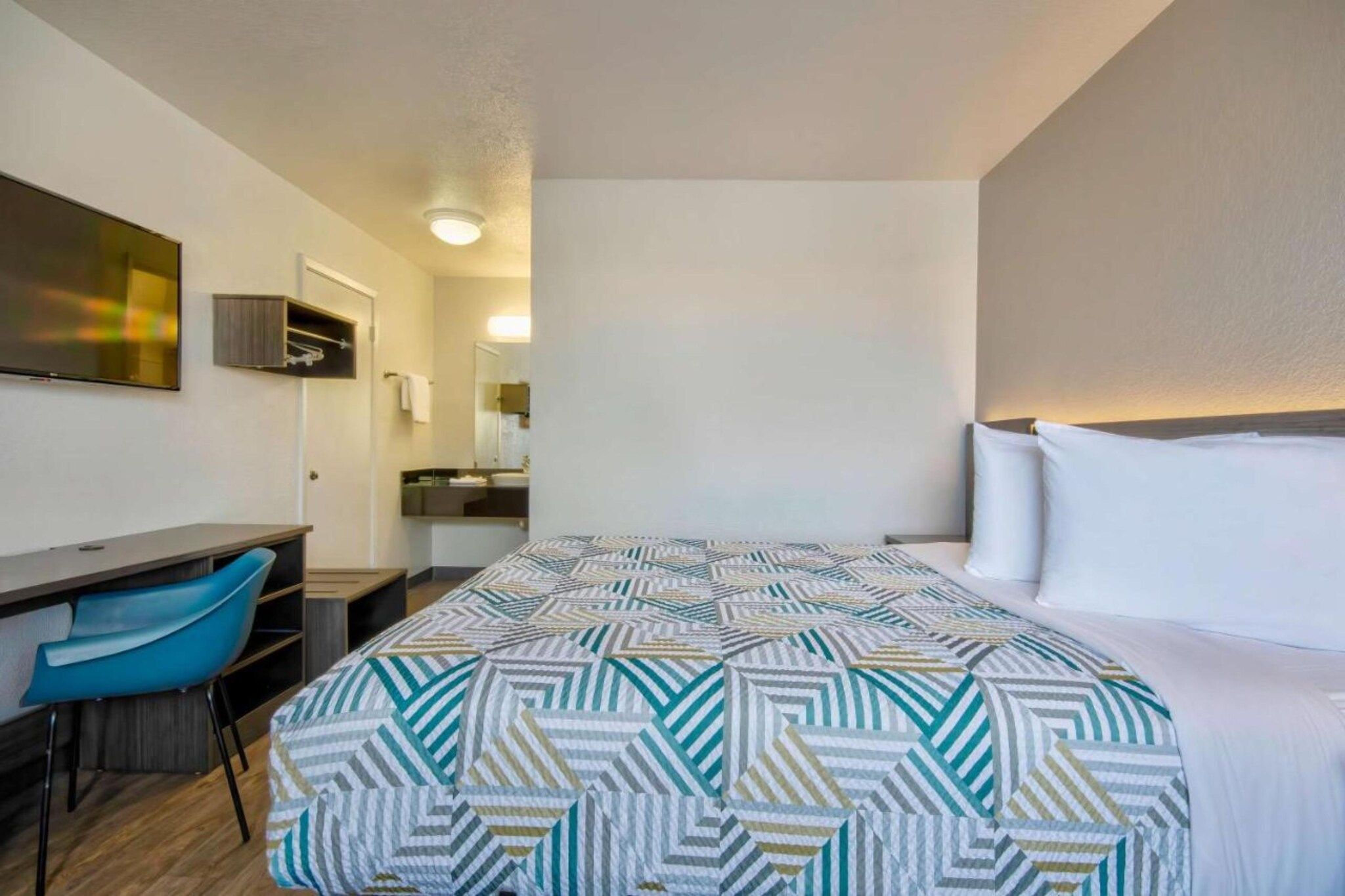 A hotel room with a bed, a desk, a chair, and a mirror.
