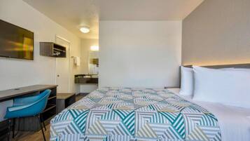 A hotel room with a bed, a desk, a chair, and a mirror.